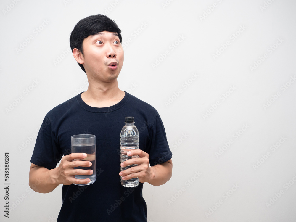 Asian man holding glass with water bottle feels excited looking at copy space Asian man holding glass with water bottle feels excited looking at copy space