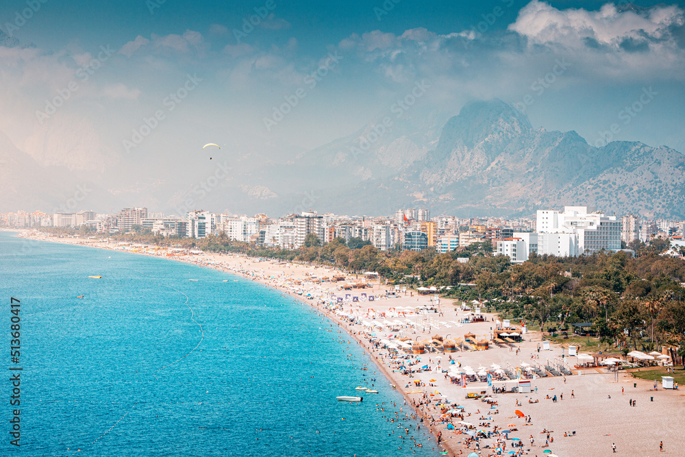 Aerial view of scenic and popular Konyaalti beach in Antalya resort town. Majestic mountains with haze in the background. Vacation and holiday in Turkiye