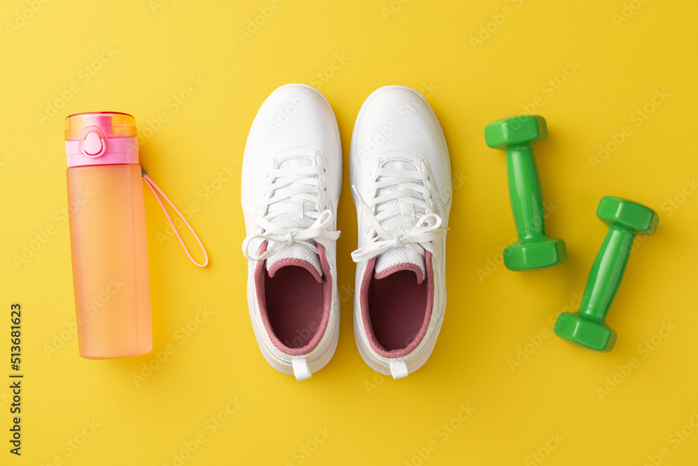 Fitness accessories concept. Top view photo of white sneakers pink bottle of water and green dumbbells on isolated yellow background
