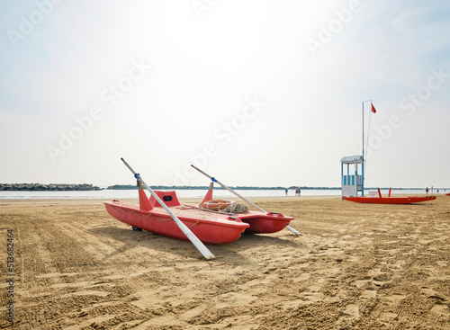 Fototapeta Naklejka Na Ścianę i Meble -  Lifeguard tower next to a lifeboat on the beach on a sunny summer morning, in the background some bathers cooling off on the Adriatic coast, Italy.
