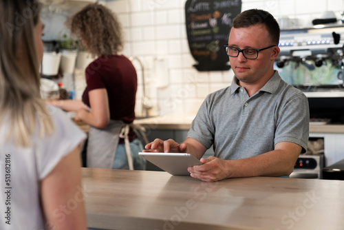 Caucasian man with down syndrome taking order in the cafe using a digital tablet