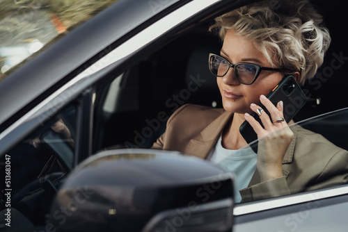 Stylish Woman in Glasses Talking on the Phone While Driving Car, Side View from Window