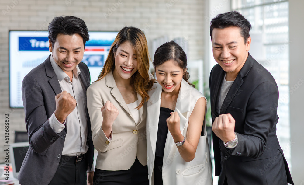 Obraz premium Group of Asian happy cheerful millennial professional successful male businessmen and female businesswomen in formal suit standing holding hands raised fists up celebrating job achievement together