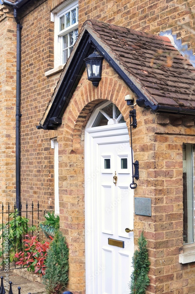 Entrance of brick old English house with white door and gold knocker in summer Entrance of brick old English house with white door and gold knocker in summer