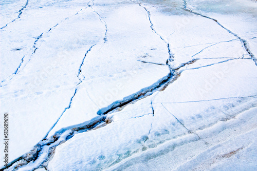 Cracks on thick ice on surface of  frozen river in winter season, powdered by snow and sand, with brilliant snow and ice crystals. photo