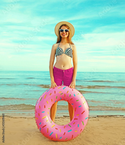 Portrait of happy smiling young woman with inflatable ring wearing straw hat on beach on sea background