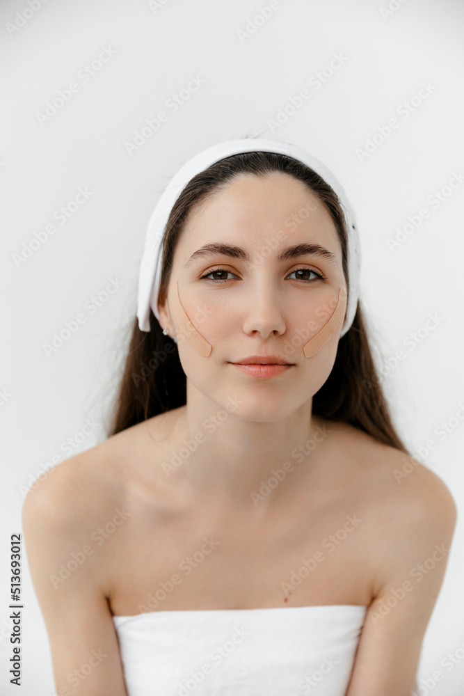 Cosmetology. beautiful young caucasian girl in the cosmetologist's office against a white background. A model with a headband and with lifting tape on her face. Kinesio taping. Cosmetology. beautiful young caucasian girl in the cosmetologist's office against a white background. A model with a headband and with lifting tape on her face. Kinesio taping.