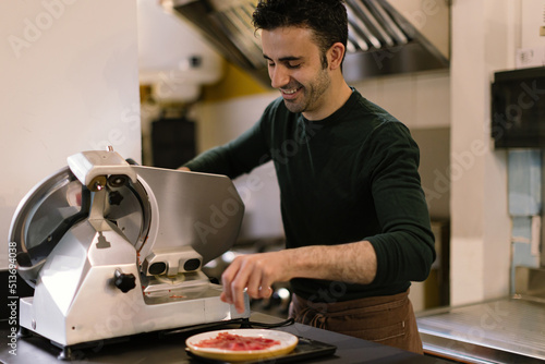 man in the restaurant kitchen preparing slices of carpaccio using the slicer photo