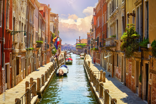 Venice, Italy. Boats, parked near brick walls of houses at street above water of channel. Sunny landscape. Summer day. © Yasonya