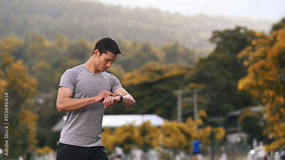 Athletic man resting and checking his heart rate data on smartwatch during morning workout in the park. Fitness, sport and healthy lifestyle concept