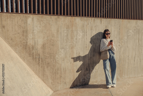 Slika na platnu Full length young caucasian woman makes purchases on Internet through phone standing against wall