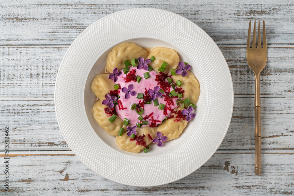 Appetizing dumplings stuffed with potatoes and mushrooms with sour cream decorated with beets and lilac flowers