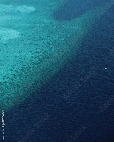 Vista aérea de un arrecife de coral del océano y de los tonos de azul con un barco pequeño navegando
