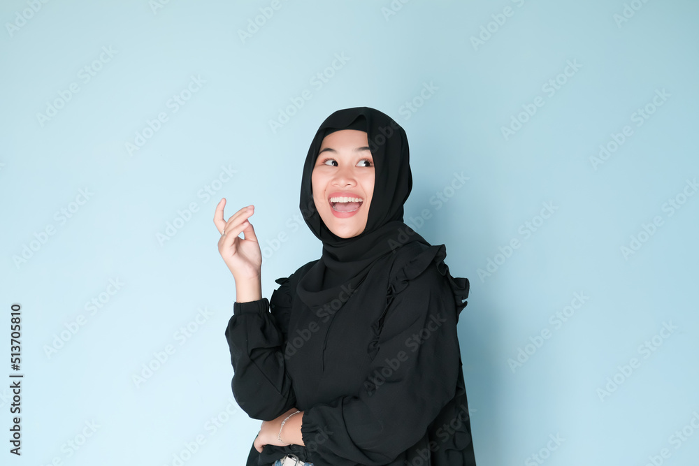 Happy expression of beautiful Asian girl in hijab in black shirt on light blue background Happy expression of beautiful Asian girl in hijab in black shirt on light blue background