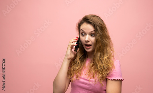 Happy surprised shocked young pretty woman speaking with a phone over pink wall background. Using mobile phone.
