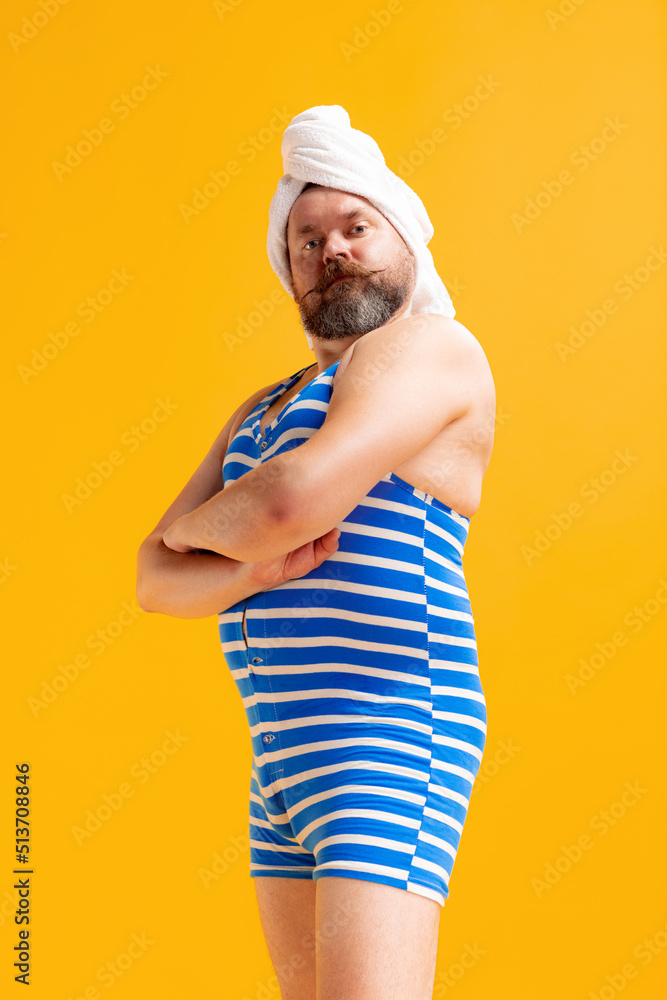 Comic portrait of funny fat bearded man in vintage style striped swimsuit having fun isolated on yellow background. Summer, beach, relax and fun time concept. Comic portrait of funny fat bearded man in vintage style striped swimsuit having fun isolated on yellow background. Summer, beach, relax and fun time concept.