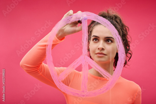 Young woman drawing pacifism sign with pink lipstick against color background photo
