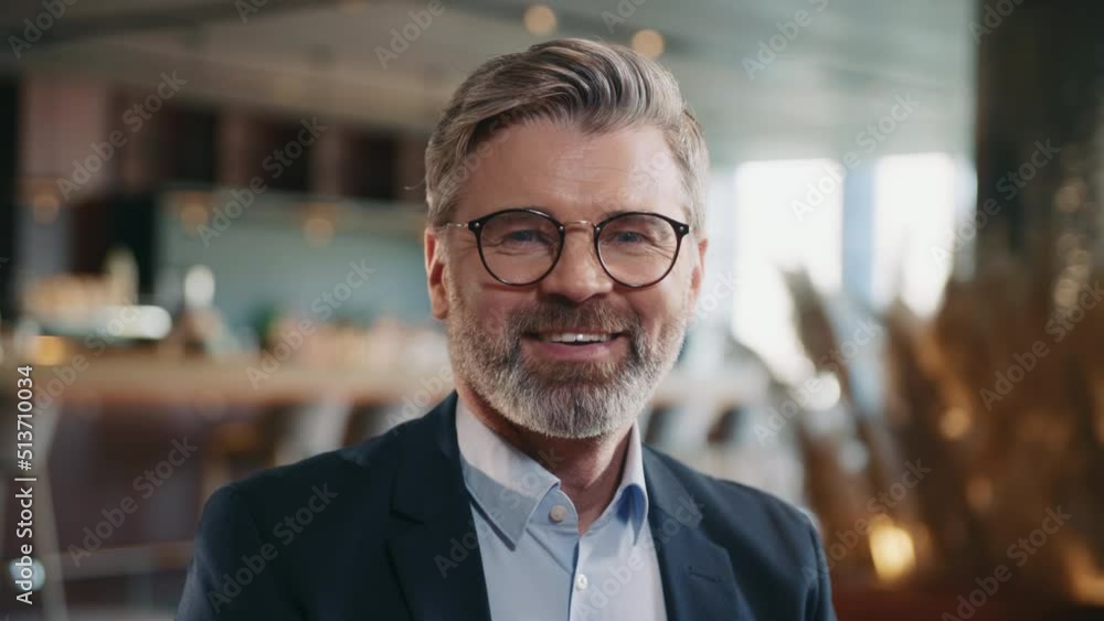 Portrait of attractive smiling Caucasian businessman in glasses looking at camera. Close-up footage of positive middle-aged man in elegant suit. Restaurant owner. Indoors. Blurred background of modern Portrait of attractive smiling Caucasian businessman in glasses looking at camera. Close-up footage of positive middle-aged man in elegant suit. Restaurant owner. Indoors. Blurred background of modern
