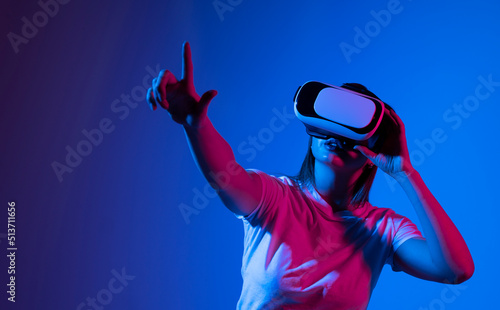 Young brunette woman wearing a virtual reality headset goggles and playing a game with a friends in metaverse. Future technology concept.
