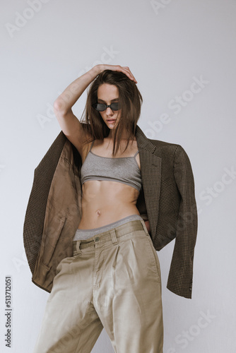 Portrait of stylish slim girl posing in sunglasses, pants and jacket isolated over grey studio background