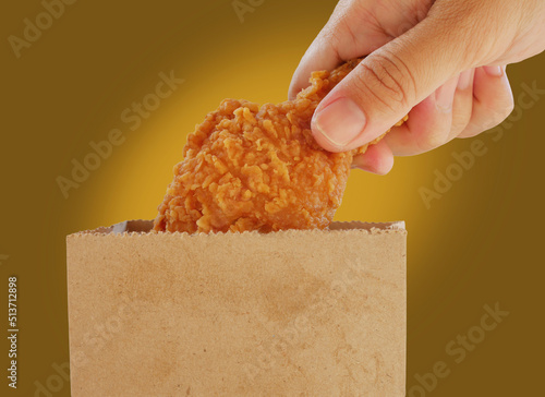 Fried chicken on this hand with paper bag of more fried chicken