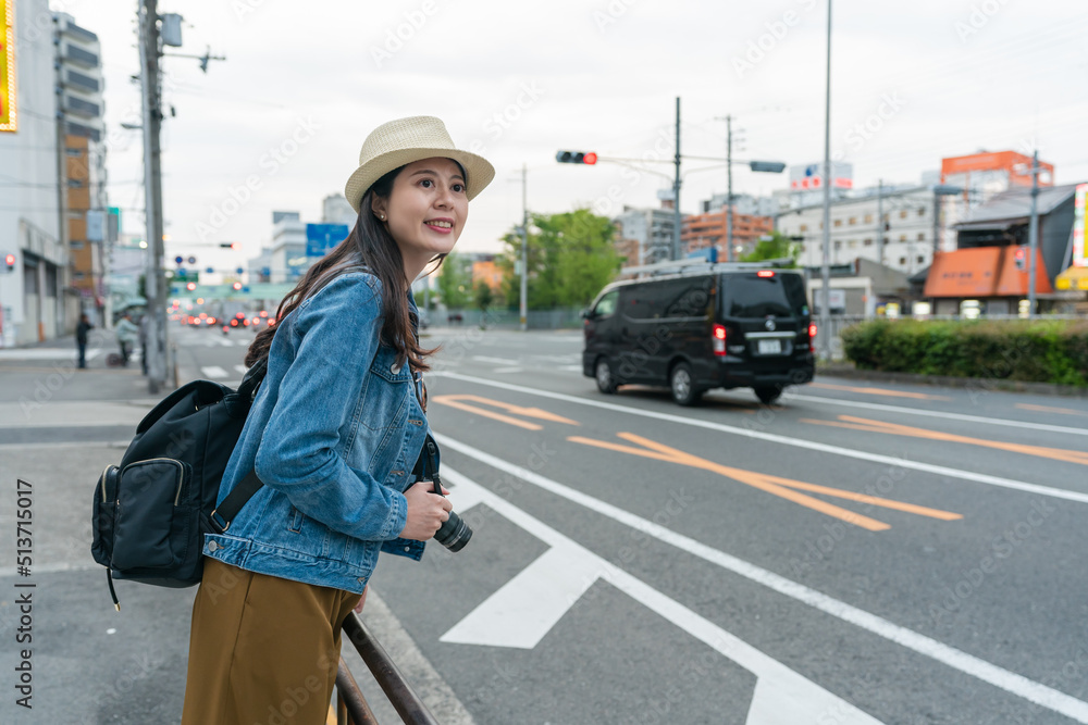 cheerful asian woman photographer wearing hat enjoying cityscape of Osaka city in japan. she looks into distance at the clean street at roadside with a smile. cheerful asian woman photographer wearing hat enjoying cityscape of Osaka city in japan. she looks into distance at the clean street at roadside with a smile.