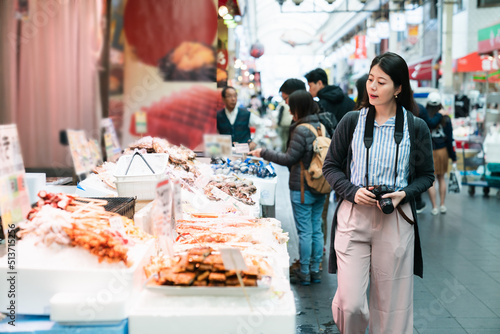 asian woman traveler with camera passing by a local stall selling Japanese processed seafood while visiting kuromon ichiba market in Osaka japan
