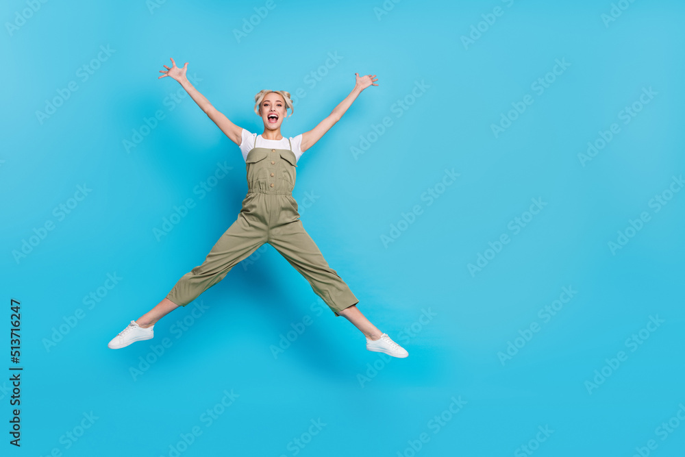 Full body photo of hooray young lady jump wear t-shirt overall sneakers isolated on blue background