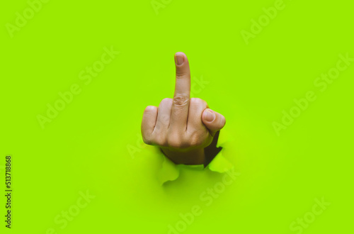 Middle finger of left hand, insulting gesture. Torn hole in green paper. Fuck you concept. Aggressive reaction. photo