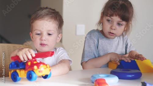 little boy and baby girl play in kindergarten. a group of children play toys cubes and cars on the table in kindergarten. happy family preschool indoor education concept. nursery baby toddler home
