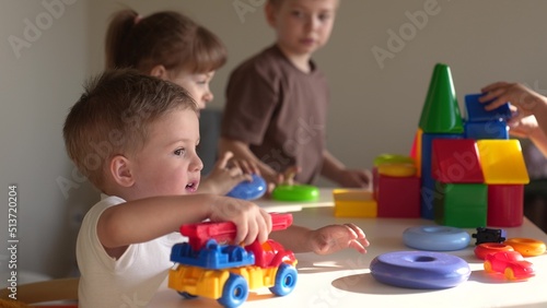 little girl and baby boy play in kindergarten. a group of children play toys cubes and cars on the table in kindergarten. happy family preschool education indoor concept. nursery baby toddler home