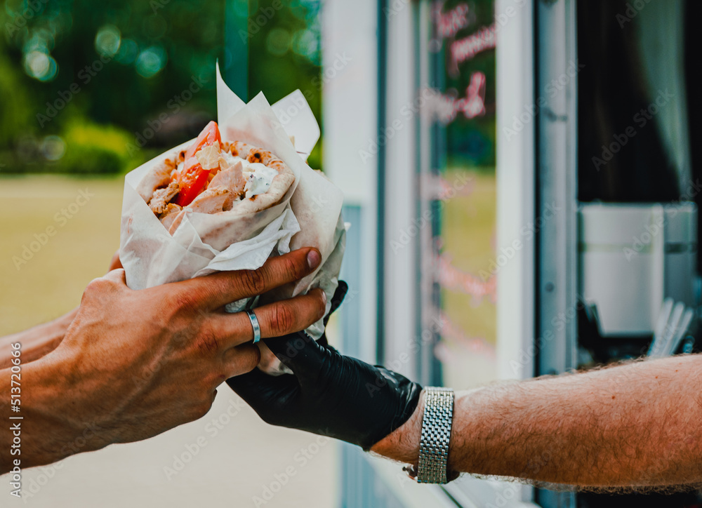 chef hands gives a gyros to man from food truck on street. street food