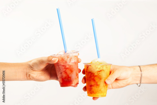 Hands holding two flavoured slush frozen drinks with straws