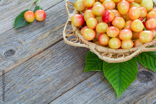 Fresh ripe berries of yellow and red sweet cherries in a wicker plate on a wooden table