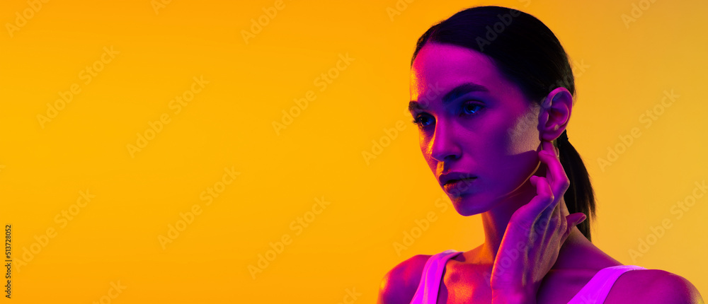 Portrait of beautiful young woman with low pony tail posing isolated over yellow studio background in neon light. Flyer