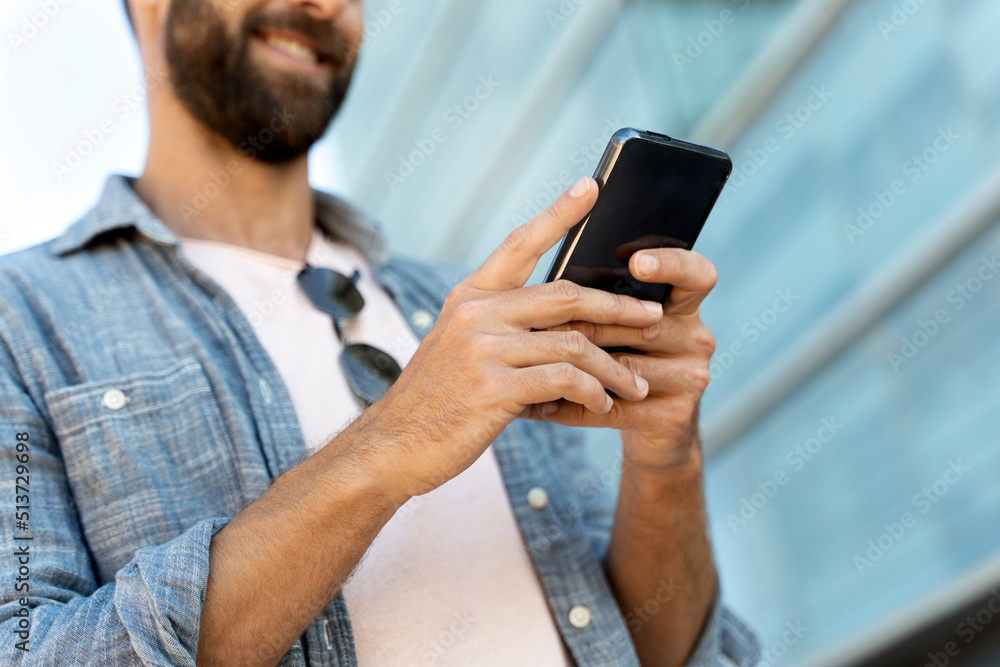 Closeup of business man hands using mobile app shopping online, sending text message outdoors. Smiling bearded hipster holding smartphone playing mobile game. Technology concept Closeup of business man hands using mobile app shopping online, sending text message outdoors. Smiling bearded hipster holding smartphone playing mobile game. Technology concept