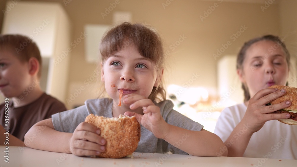children eat burgers. fast food burger. a group of small children in the kitchen fun greedily eat fast food burgers. big family small kids having breakfast in the morning in the kitchen eating burger