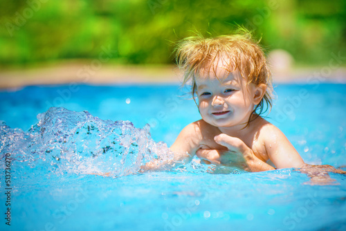 The baby is learning to swim. The child has fun outdoors in the pool in the villa. Family happiness. Little beautiful girl is splashing in the pool © watman