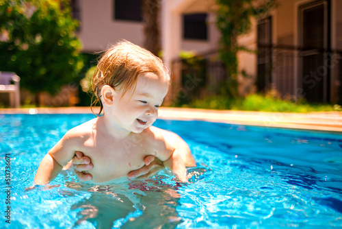 The baby is learning to swim. The child has fun outdoors in the pool in the villa. Little beautiful girl is splashing in the pool. Family happiness © watman