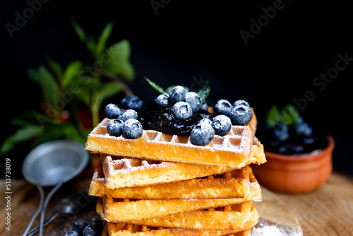 Waffles with fresh blueberries and powdered sugar on the rustic table. Freshly made Belgian waffles