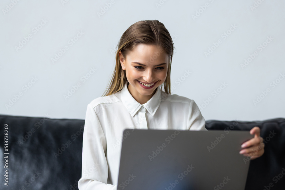 Relaxed woman using laptop in luxury home living room with big window, enjoying working, internet shopping, checking social network with computer sitting on sofa Relaxed woman using laptop in luxury home living room with big window, enjoying working, internet shopping, checking social network with computer sitting on sofa