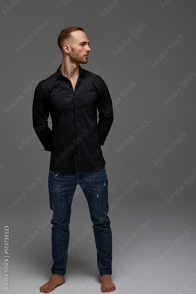 An attractive white man in jeans and black shirts tands in full growth against a gray background. Copy space An attractive white man in jeans and black shirts tands in full growth against a gray background. Copy space