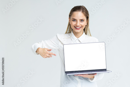 Business woman smile sitting at the desk looking at camera, point finger at isolated white laptop screen over white background