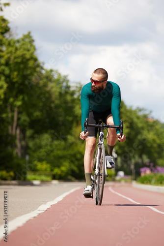 Portrait of a sporty man in a cycling outfit standing with a bicycle on the Bike Lane, posing for the camera © Georgii