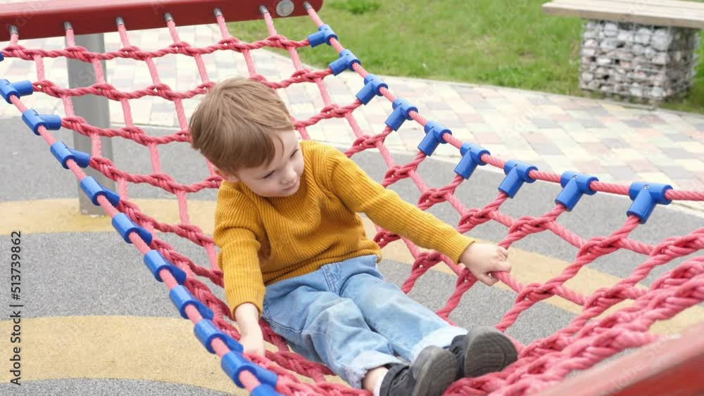 Happy child, swinging in a hammock, on the playground, during children's entertainment on the street. Happy free childhood Happy child, swinging in a hammock, on the playground, during children's entertainment on the street. Happy free childhood