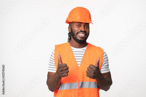 Happy african-american young man engineer construction worker architect in orange reflective vest and hardhat looking at camera showing thumb up isolated in white background