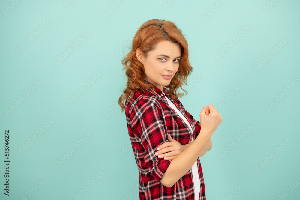 smiling redhead woman in checkered shirt threatening with fist on blue background smiling redhead woman in checkered shirt threatening with fist on blue background
