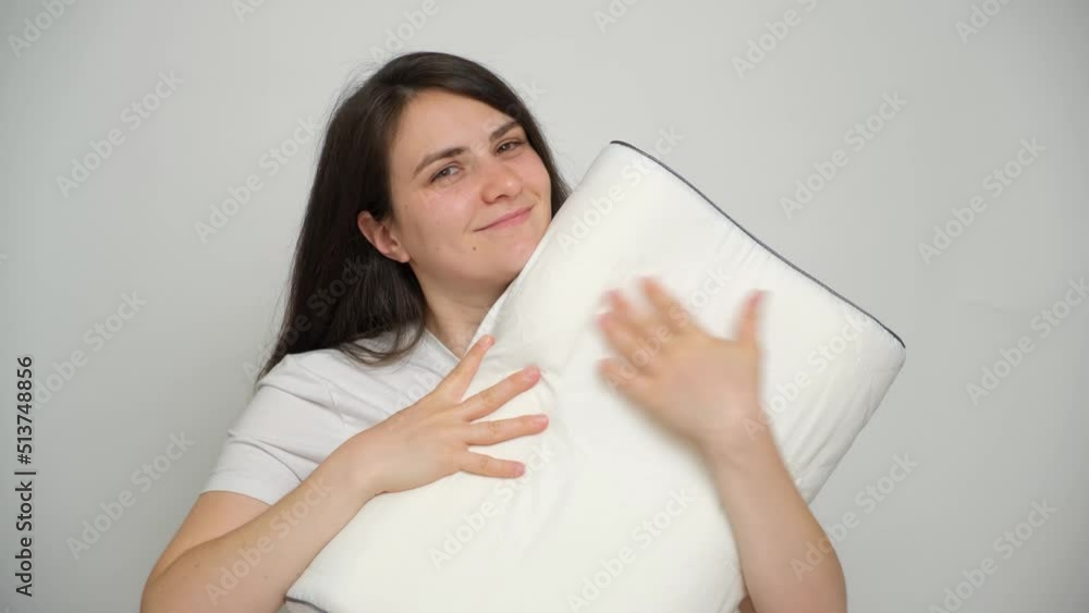 A woman hugs her favorite orthopedic white pillow and smiles as she looks into the camera A woman hugs her favorite orthopedic white pillow and smiles as she looks into the camera