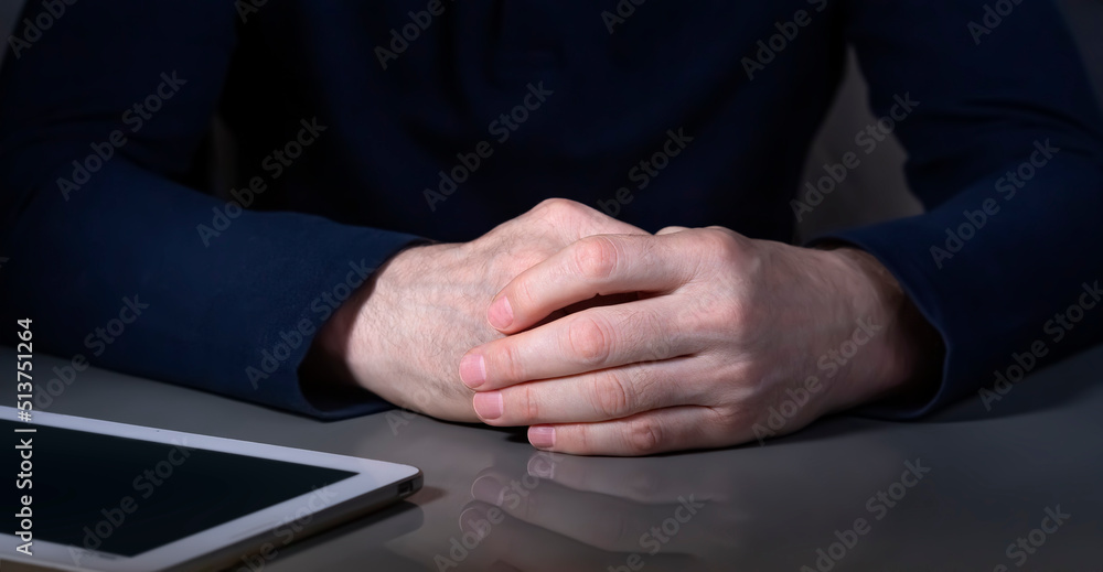The hands of a mature businessman with a tablet in dark colors