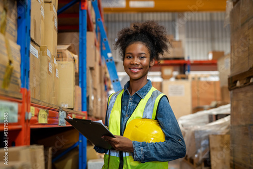 Portrait of female staff smiling with holding clipboard standing in warehouse with looking at camera, Industrial and industrial workers concept.